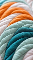 Close-up of a colorful quilted fabric with a rainbow pattern. The fabric features various shades of orange, white, teal, and blue, creating a textured and visua