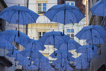 Art installation of hanging blue umbrellas with fairy lights in an alleyway. A low-angle view of a creative art installation