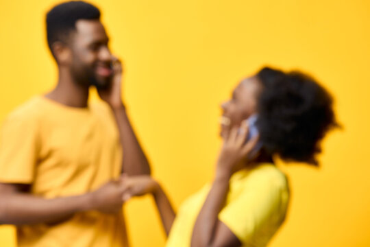 Happy couple on phone talking together against a bright yellow background, wearing casual clothing, expressing joy and connection in a vibrant summer setting