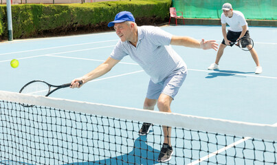 Portrait of concentrated elderly man playing tennis with friend on court.