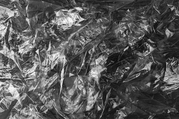Black and white crumpled plastic texture with reflective wrinkled surface creating abstract glossy material background. 