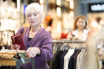 Customer inspect at products in store and pick out clothes, accessories. Mature woman search and choose wallet, purchase some wardrobe items. Style and fashion type look, modern trends.