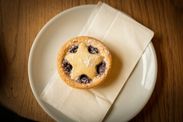 A festive mince pie with a star-shaped pastry top sits on a white plate with a napkin, ready to be enjoyed as a holiday treat.
