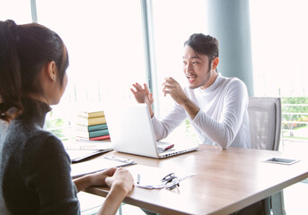 A lively business discussion between two colleagues in office. Asian man explains ideas with expressive gestures, positive atmosphere suitable for teamwork and professional communication.