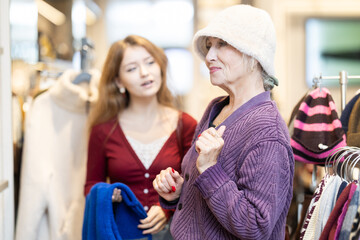 Positive young girl and mature woman trying warm hat in clothing shop with large assortment