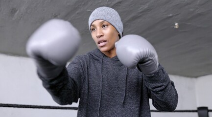 Determined Woman Boxer Training in Ring with Gloves and Beanie, Ready for Action and Physical Fitness.