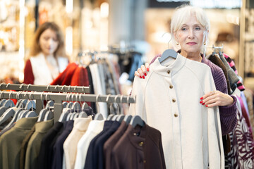 Selective old female customer looking for autumn outerwear in fashion retail outlet