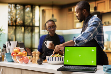 Isolated mockup laptop next to couple doing meal prep in the kitchen, man and woman cooking and spending time together at home. Happiness and healthy lifestyle, bonding with joy.