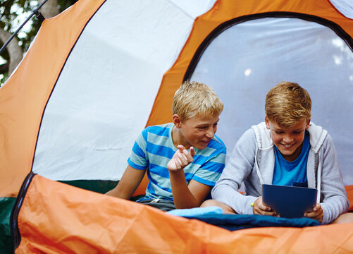 Kids, tablet and boys in tent, smile and typing with online game, relax and entertainment. Camping, friends and children with technology, happiness and internet with fun, bonding together and network - Powered by Adobe