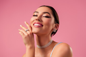 Gorgeous young woman with elegant diamond jewelry poses confidently against pink background