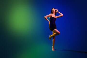Elegant young woman posing against vibrant neon lights background with dynamic green and blue color gradients