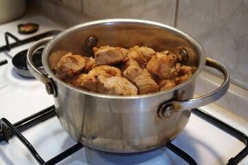 Meat is stewing. There is a pot of meat on a gas stove