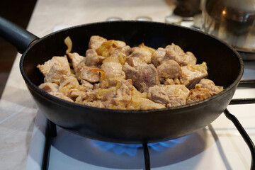 Frying meat. Pieces of meat with onion in frying pan on gas stove