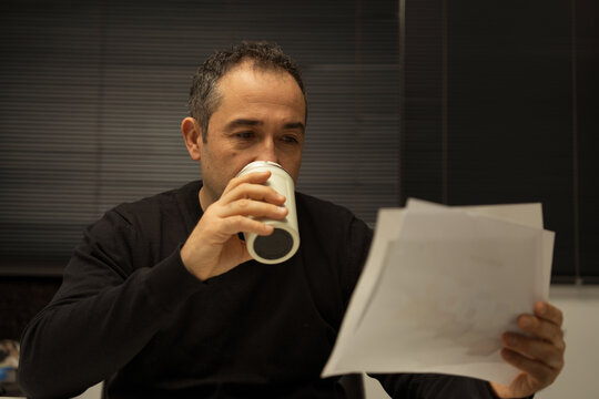 Man drinking coffee reading documents in office