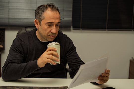 Focused businessman reading documents and drinking coffee in office
