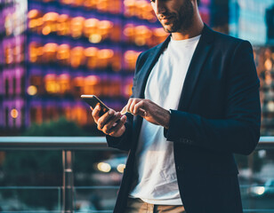 Stylish man uses smartphone with cityscape bokeh. Business, technology, modern lifestyle. Perfect for finance, travel, or communication concepts.