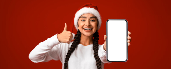 A cheerful woman with braided hair and a Santa hat stands against a vibrant red background. She...