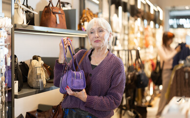 Undetermined young female customer looking for shoulder bag in fashion retail outlet