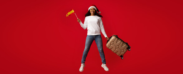 A cheerful traveler dressed in a festive outfit jumps with excitement holding a suitcase and waving...