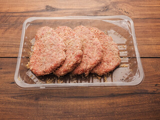 Lamb uncooked steak coated in Arabic Harissa style herbs and spices in plastic tray on wooden table. Red minced meat. Fine butcher style burgers ready for cooking.