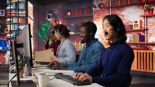 Call center operator next to coworkers dealing with upset customers, speaking using headset at office desk. Teamworking staff members doing customer support job, handling clients complaints, camera B