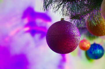 Colorful Christmas decorations hanging on a Christmas tree branch with bright purple and pink holiday lights. Background with shiny balls, and bright bokeh, Christmas and New Year background with ball