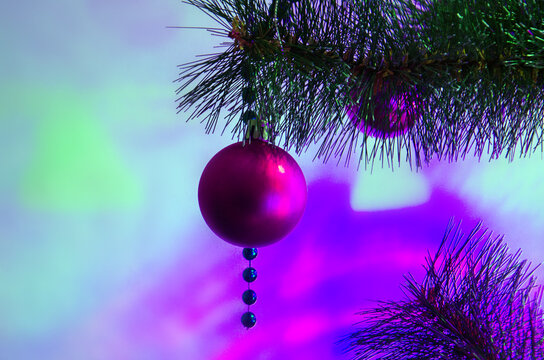 Christmas decoration hanging on a Christmas tree branch with bright purple and pink holiday lights. Background with purple Christmas ball, and bright bokeh, Christmas and New Year background with ball - Powered by Adobe