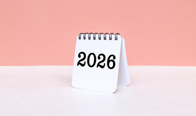 White calendar 2026 on the desk isolated pink background. New Year 2026 Calendar on the table surrounded by books, cups, plants. Beginning with Purpose and Future Planning