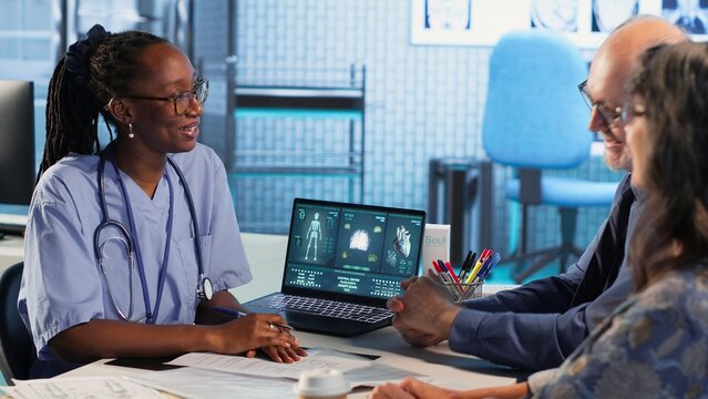 Medical assistant consulting couple of patients about test results and MRI scans, reviewing records to create the diagnostic report. Patient care management in a medical cabinet. Camera B. - Powered by Adobe