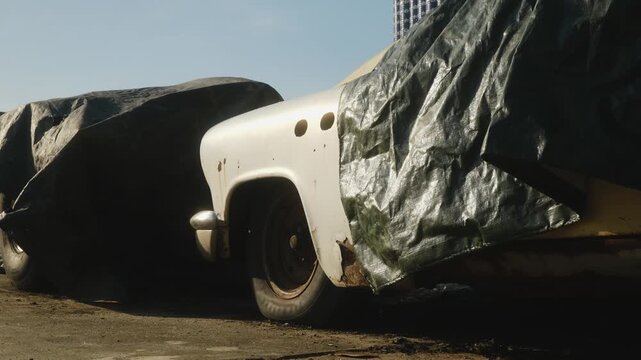 Close-up of a vintage white automobile with rust damage hidden under a plastic cover, representing abandoned projects, restoration, or automotive history.