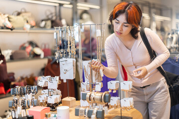 Young Asian woman stands near a jewelry counter and chooses a necklace. Buying fashionable jewelry in the store with accessories in the shopping center