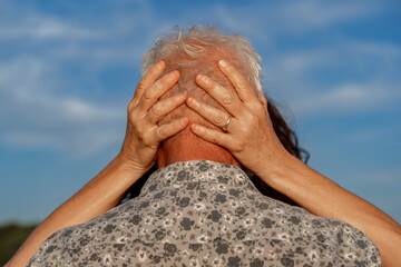 Senior woman's hands tenderly caressing man's head against a blue sky