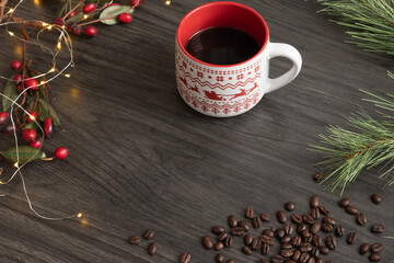 Cup of coffee with a festive border of lights, evergreen branch and red berries