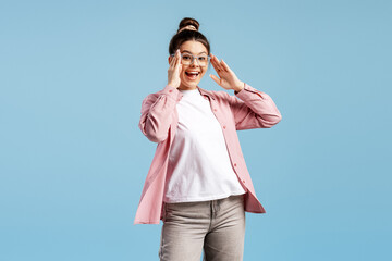 Ecstatic young woman in glasses reacting to surprising news with open mouth