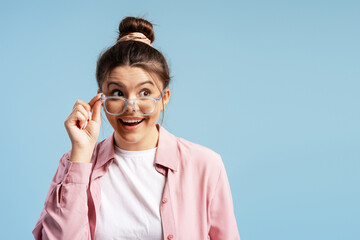 Young woman raising glasses, showing curiosity and surprise on a blue background