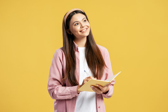 Young woman writing notes in notebook, finding inspiration on yellow background