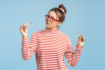Young woman pondering options, holding multiple pairs of glasses, looking unsure