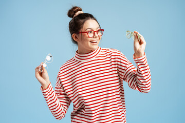Young woman smiling, holding two pairs of eyeglasses, choosing the perfect fashion accessory