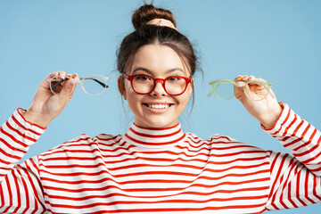 Young woman choosing corrective glasses, comparing different frame styles for vision care