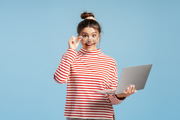 Amused young woman holding laptop and adjusting glasses, feeling surprised