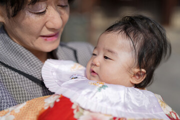 A woman is holding a baby in her arms. The baby is wearing a white collar
