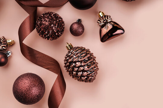 Bronze Christmas ornaments, baubles, pinecone and ribbon arranged on pastel nude background with copy space