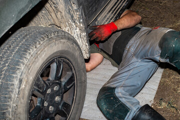 A car mechanic, lying under the bottom of a car, carries out maintenance on the car's suspension without using a lift