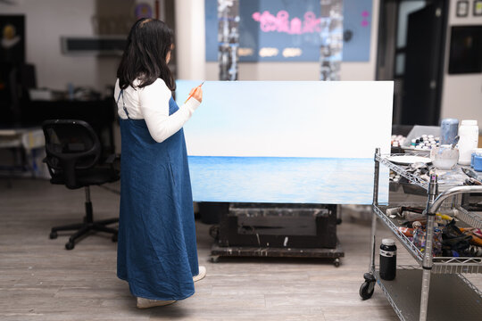 Female artist painting a blue seascape on a large canvas