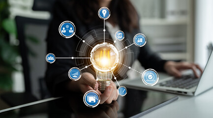 This image depicts a business professional holding a light bulb surrounded by digital icons, symbolizing innovation and creativity in a modern office setting. Crux