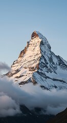 Snow capped mountain peak illuminated by golden sunlight above clouds summit rock