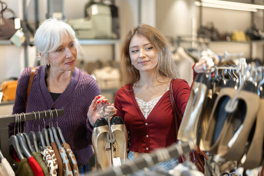 Positive young girl and mature woman choosing shoes in clothing shop with large assortment