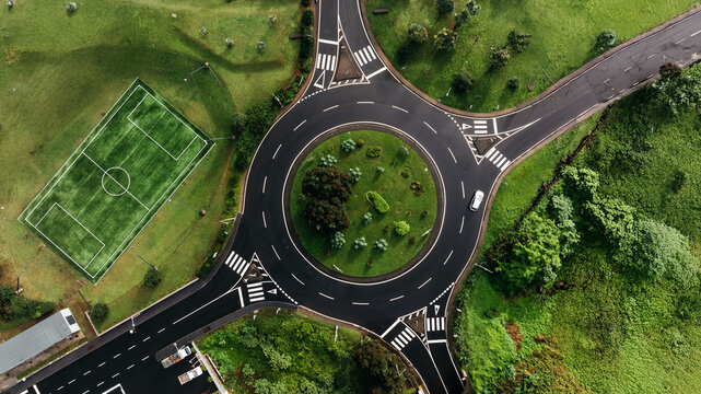 Aerial view of a circular intersection surrounded by lush greenery, featuring a soccer field nearby, illustrating urban planning and nature integration in a vibrant landscape