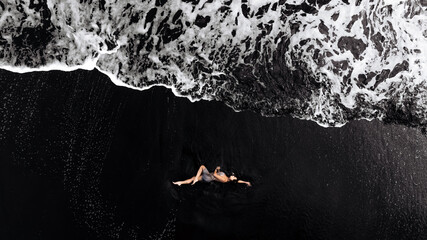 Woman relaxing on dark beach, surrounded by foamy waves, capturing a serene moment of tranquility and connection with nature, evoking feelings of peace and escape