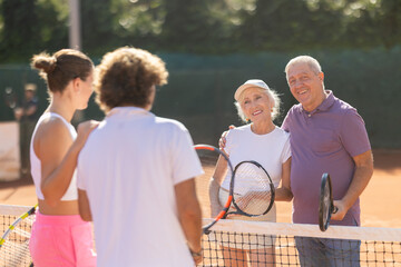 Married couple chatting with mature couple after playing tennis. Group of friends spend time together playing tennis in the outdoor court